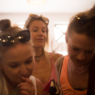 A group of three women standing close together, looking at something with interest. The lighting is soft and inviting, creating a cozy and friendly atmosphere.