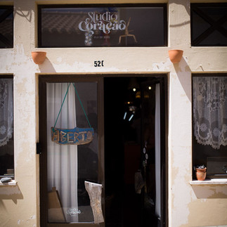 Exterior view of the Studio Coração entrance, showing the sign “Aberto” (open) on the door and a rustic appearance with peeling paint on the facade, adding to the studio’s character.