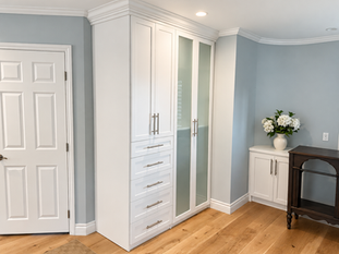 White built-in wardrobe with glass-panel doors and drawers in a gray-blue bedroom