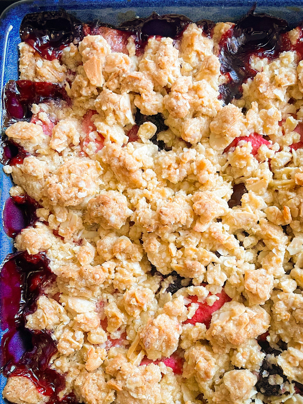 Gluten free apple and blackberry crumble in a blue dish, photographed from above.