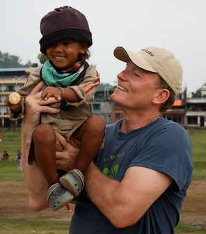 Trevor Ironside lifting young Nepali child up high. Both are smiling.