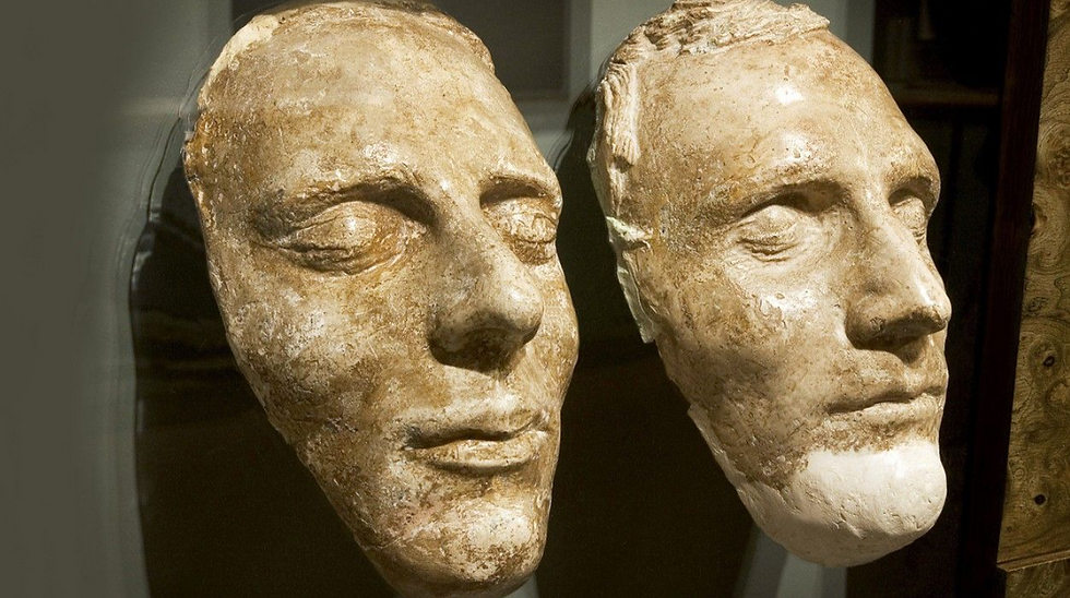 Two plaster face masks with serene expressions displayed against a dark background; both feature closed eyes and a beige, textured surface.