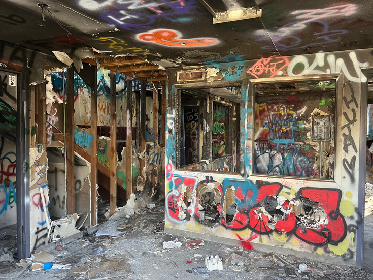 An abandoned building covered in graffiti, with a staircase on the left, and holes in the walls.