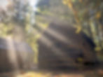 A rustic log cabin in the Mount Hood National Forest with rays of sunlight shining down from a blue sky