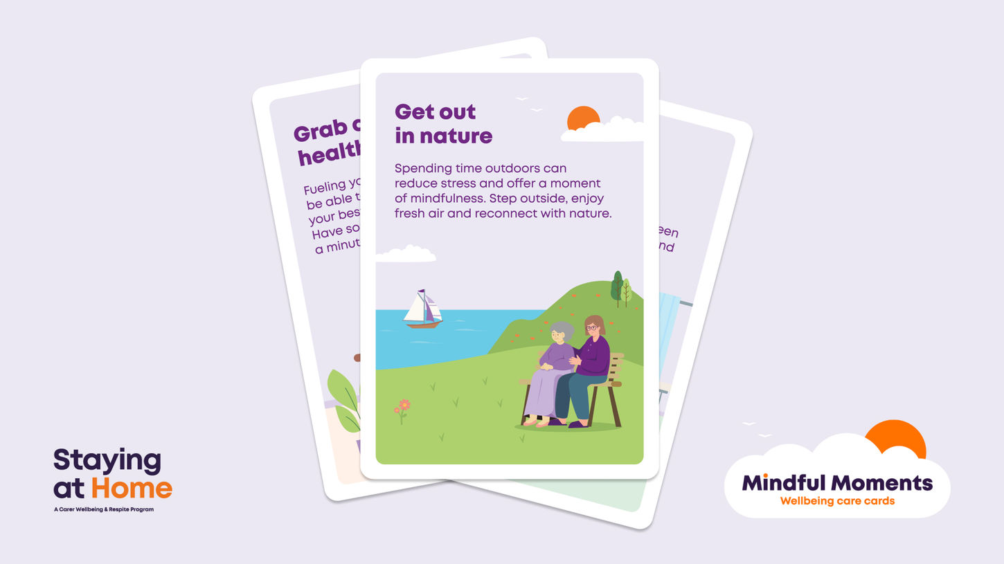 The “Get out in nature” card in front of two other cards. Its illustration shows two older people sitting on a bench overlooking the sea and a sailboat, beside the “Staying at Home” and Mindful Moments logos.