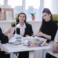 A group of four women sitting around a desk in a bright office, discussing work and reviewing documents together.