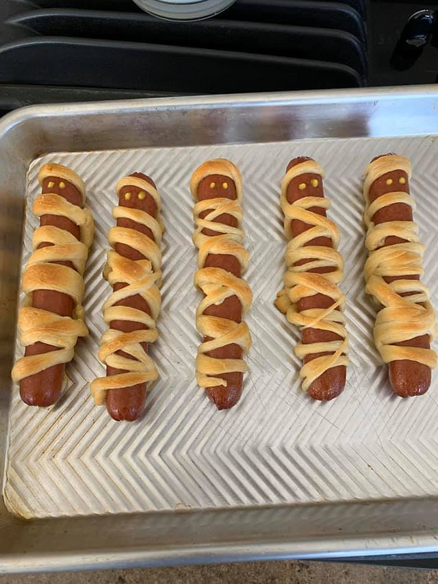 Golden baked mummy hot dogs wrapped in crescent dough, fresh from the oven with mustard eyes.