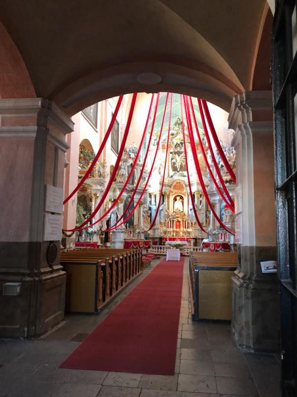 Ornate church interior in Lithuania decorated with red ribbons leading to the altar, prepared for Vincentas’ baptism.