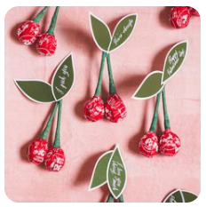 Valentine’s Day cherry-themed lollipop craft arranged on a pink background with green paper leaves