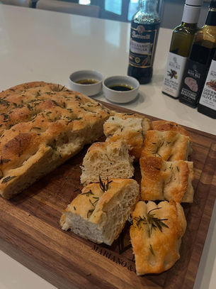 Golden-brown focaccia bread topped with rosemary and sea salt, served with dishes of olive oil and balsamic vinegar for dipping