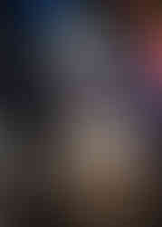 Fearless Girl Statue in the foreground looking toward a brightly lit Christmas tree on wall street at night.