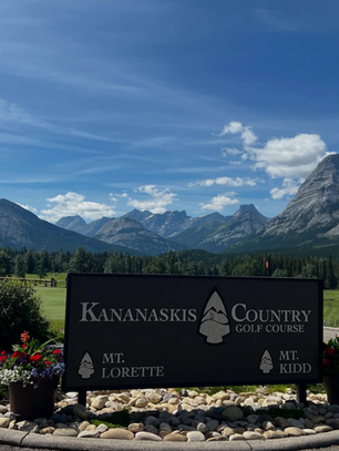 Scenic view of the Canadian Rockies at Kananaskis Country Golf Course with mountains, blue sky, and welcome sign surrounded by flowers.