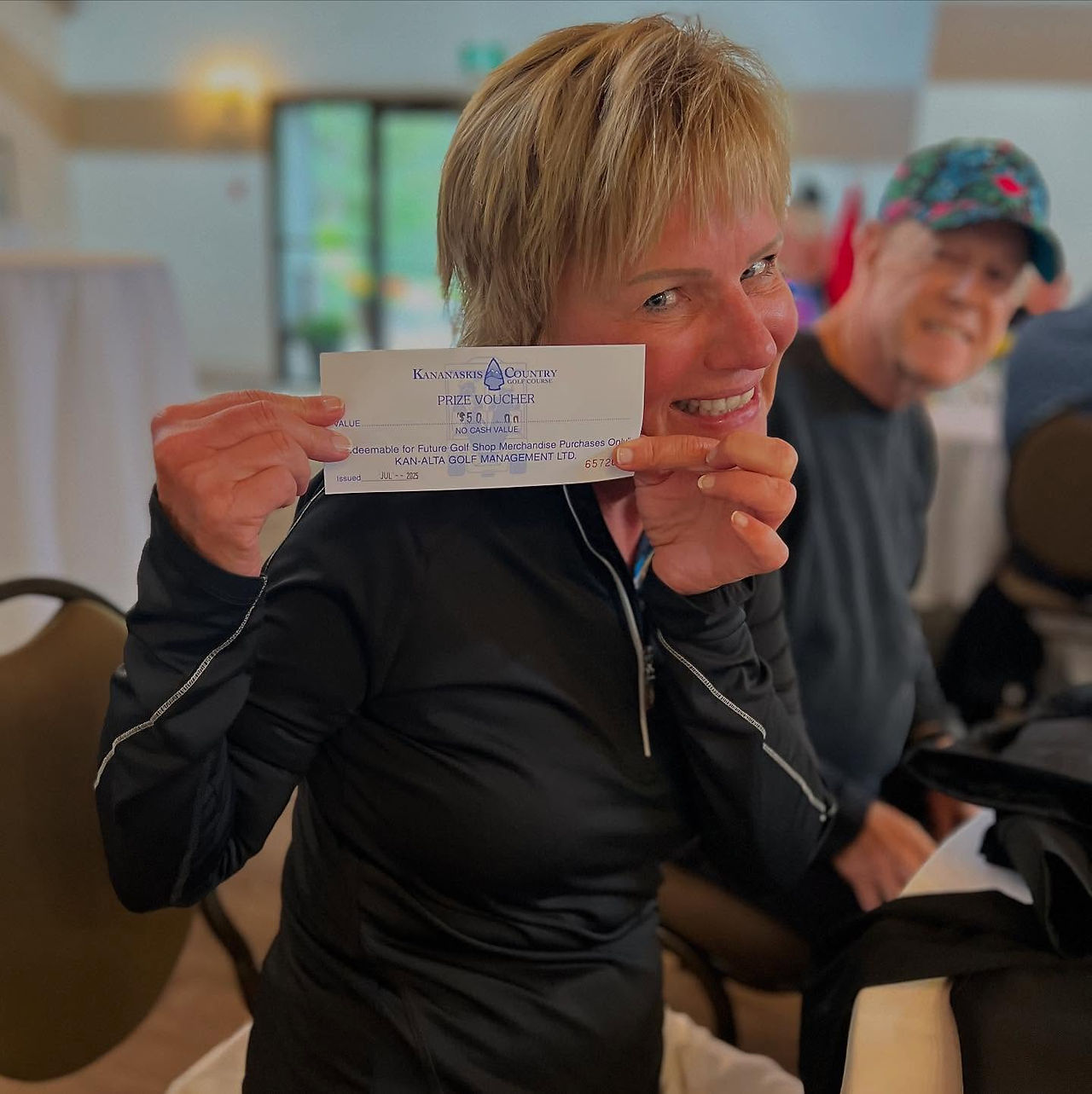 Tammie's friend smiling proudly holding a certificate during a golf tournament event in Kananaskis.