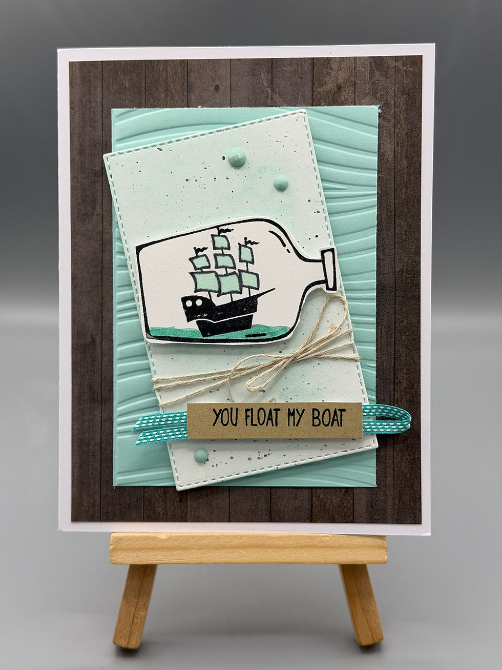 “Handmade nautical greeting card with ship-in-a-bottle design, twine bow, and message ‘You Float My Boat.’”