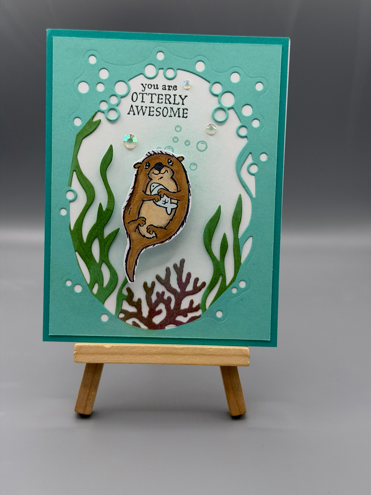 Handmade greeting card featuring a cute otter holding a seashell with “You are Otterly Awesome” message and underwater design