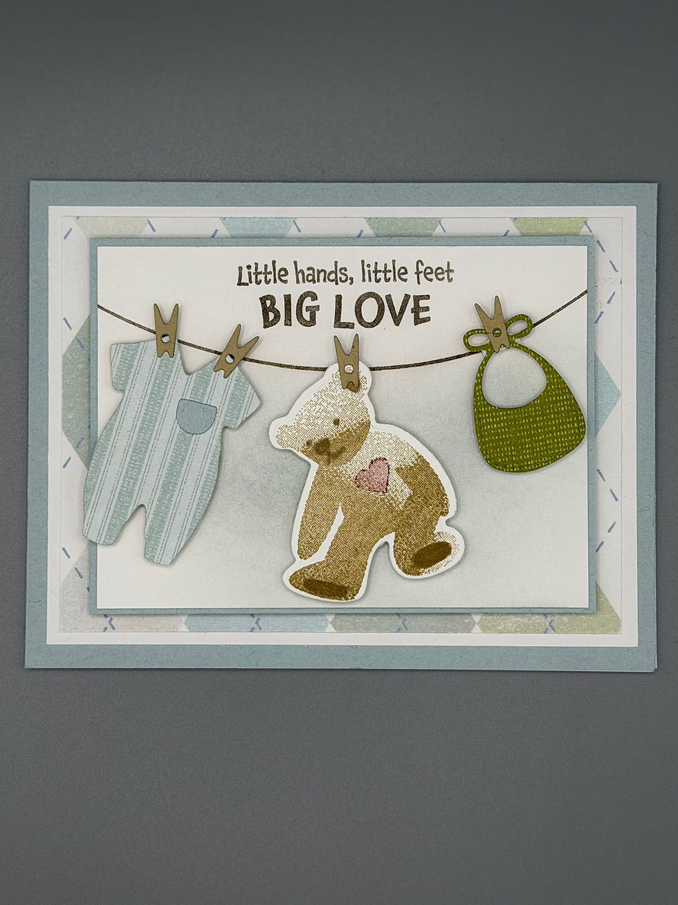 Thumbnail: “Baby-themed card with pastel blue and green layers, featuring teddy bear and baby clothes cutouts.”