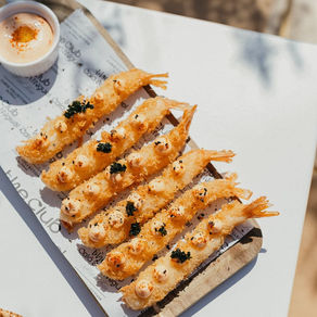 Unas gambas rebozadas en una foto cenital en un hotel en ibiza con una luz directa del sol dura con unas sombras de un olivo dan un toque veraniego y fresco