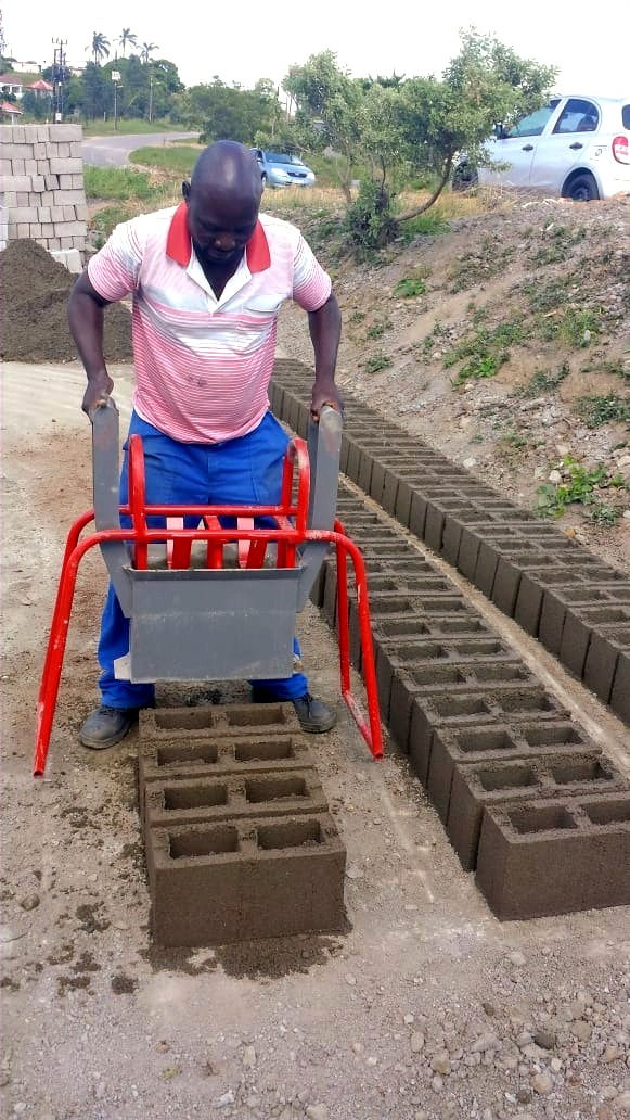 A brick-maker is lifting the hand mould off of a freshly-made M6 cavity block