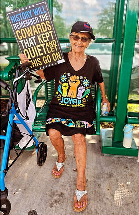 Woman holds sign: "History will remember the cowards..." outside, HOME.