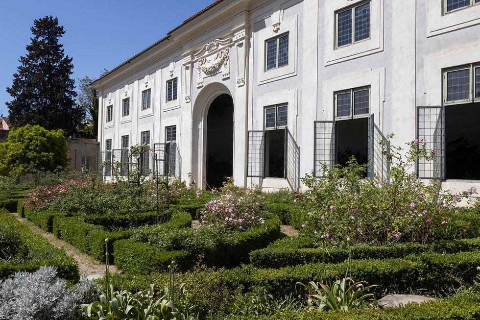 An ornate barn with open windows and a knot rose garden in front