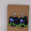Thumbnail: drop earrings of a black square bookshelf with a black cat purple and blue books and potted ivy plant
