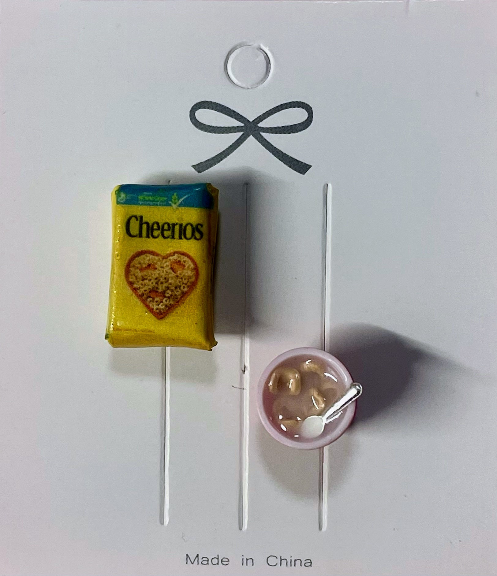 lapel brooch and pin of a cheerios cereal box and a bowl of cereal with a tiny spoon  in it