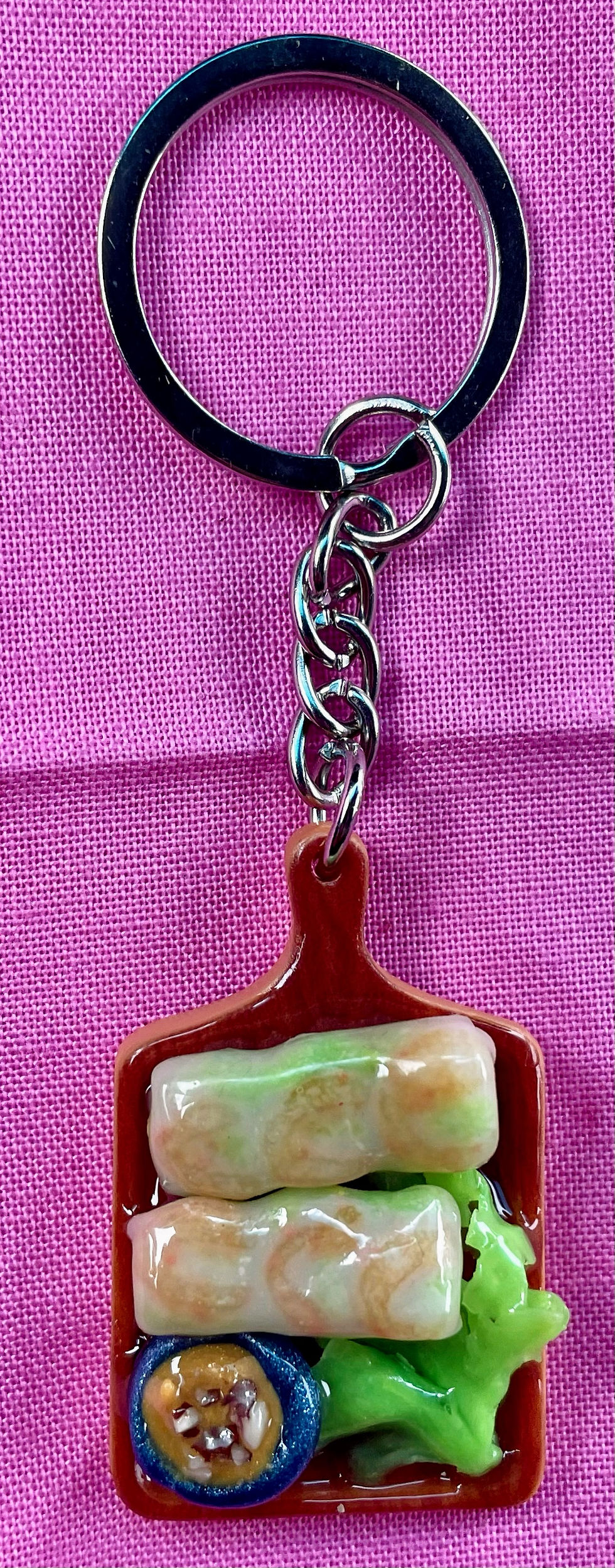 Keychain of shrimp spring rolls  and peanut sauce dip with nuts in a blue dipping bowl on a wood cutting board and lettuce