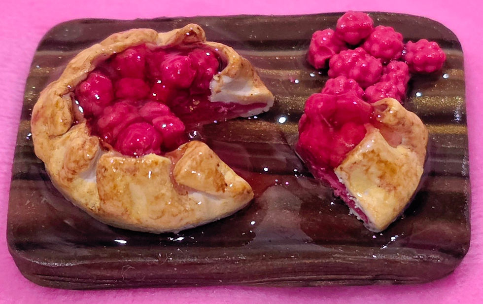 Close-up of a miniature raspberry pie food magnet showing realistic baked crust texture and glossy raspberry detail