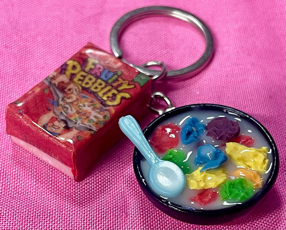 keychain of a fruity pebbles cereal box and a bowl of cereal with a colorful spoon  in it