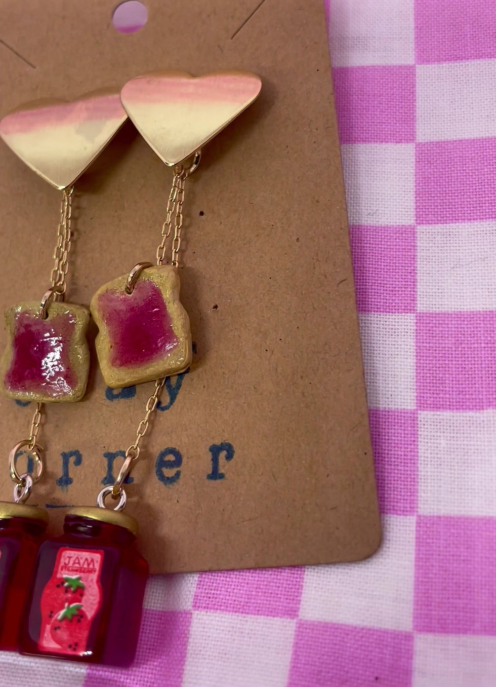 Thumbnail: Drop earrings of a gold heart with two chains hanging from each earring and each chain contains a jar of strawberry jam and a