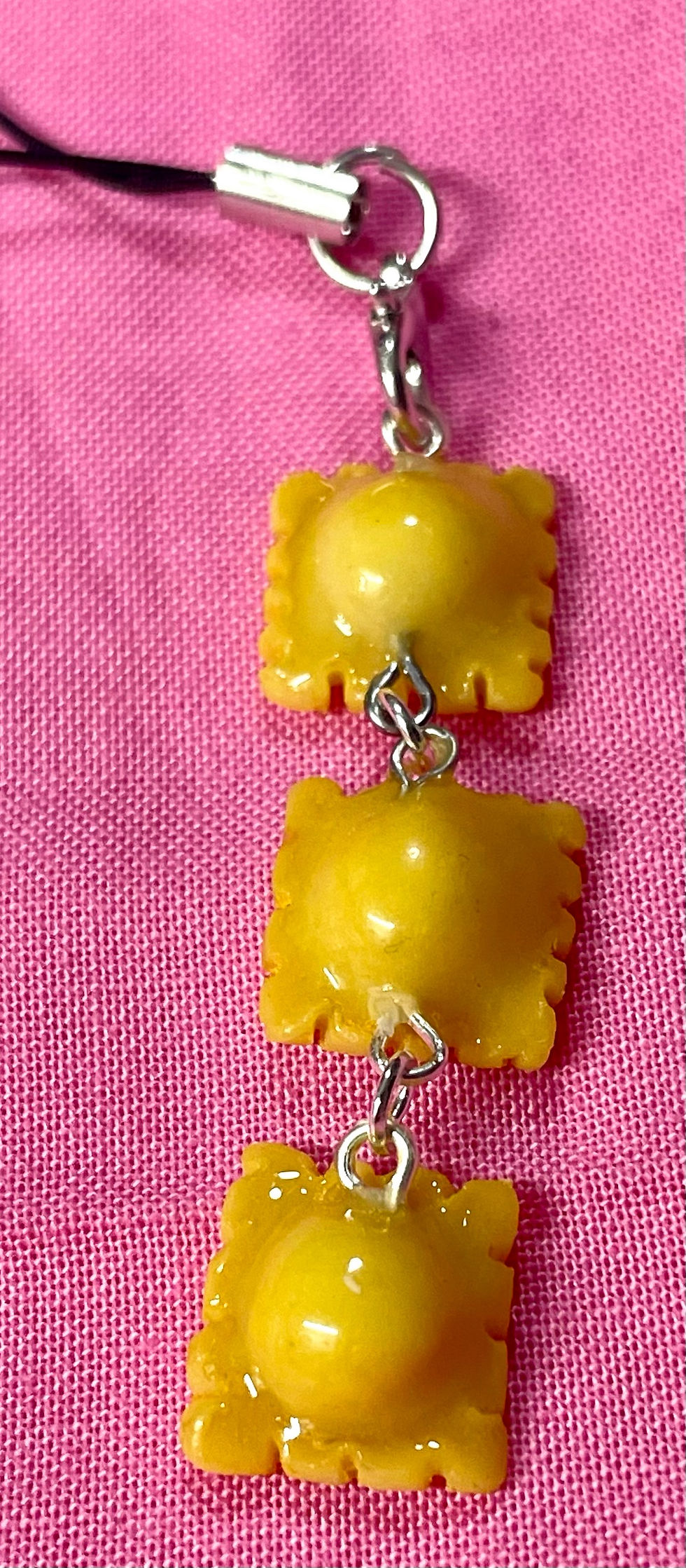 Thumbnail: phone charm of three cooked yellow raviolis hanging from each other