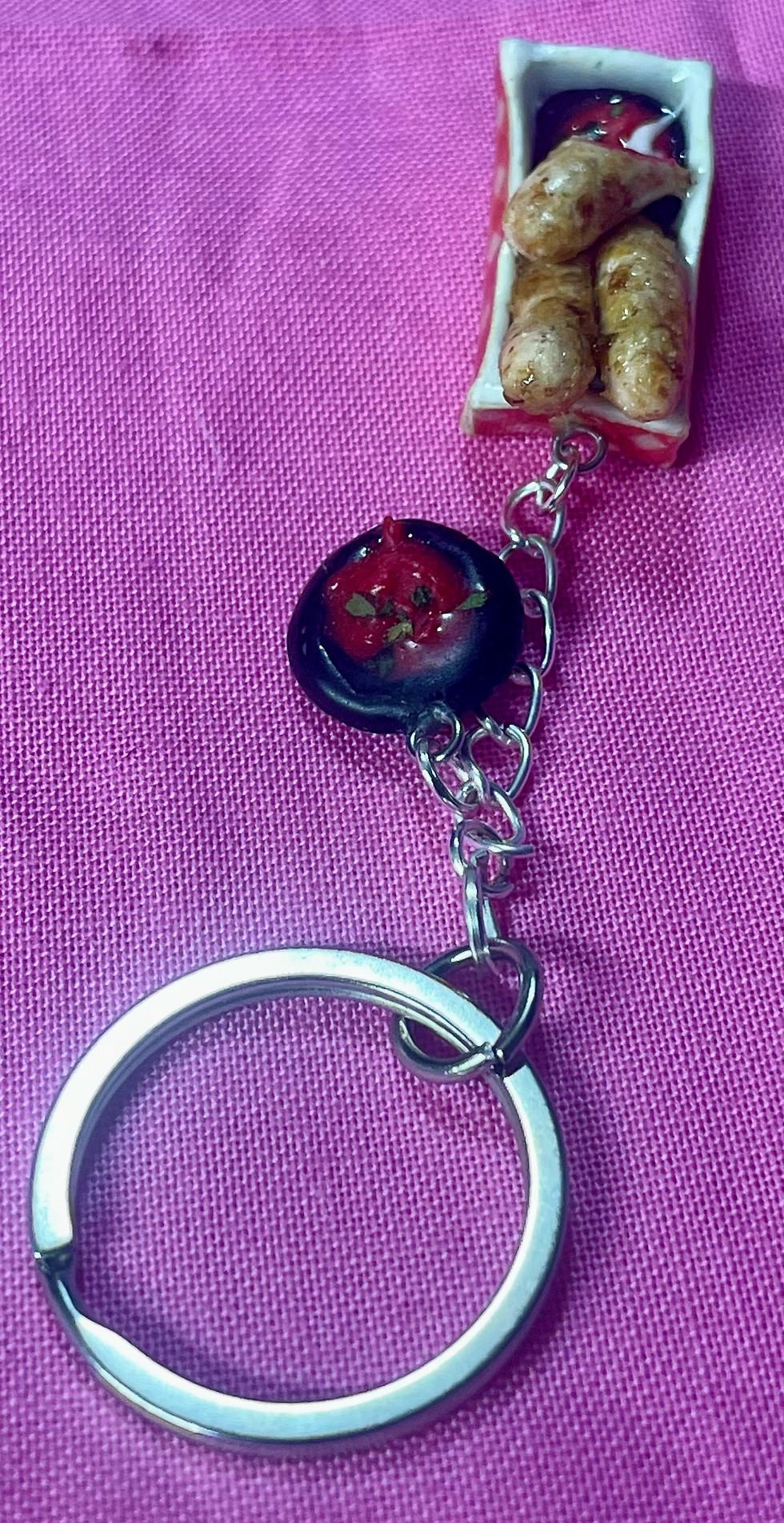 Thumbnail: keychain of 3 mozzarella sticks , one half eaten and dipped in marina sauce and a pin of marinara sauce in a black dish