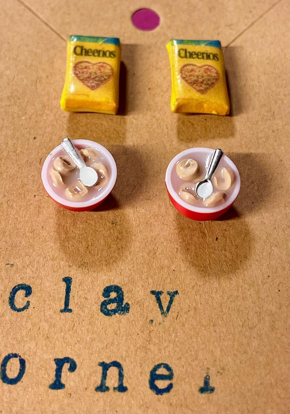 2 pairs of stud earrings of cheerios cereal boxes and a bowls of cereal with a tiny spoon in it