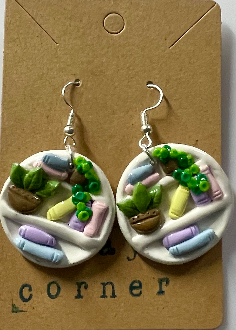 earrings of a circular white bookshelf and inside are plants and a pink blue yellow and purple books