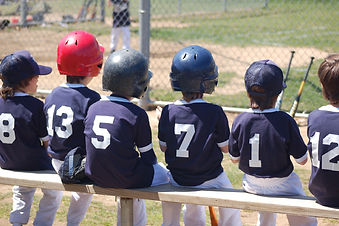 an image of a co-ed kids baseball team with players sitting on a bench waiting to hit