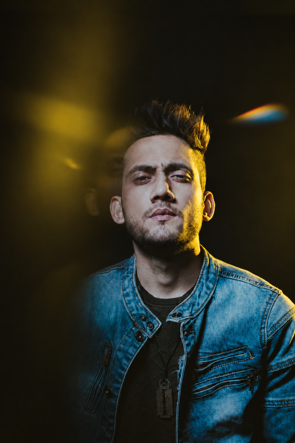 Danish Qamar in a blue denim jacket, lit by yellow light against a dark background.