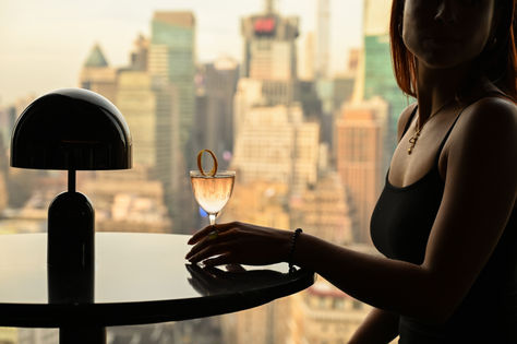 Elegant cocktail held by a woman at a rooftop bar with a panoramic NYC skyline backdrop—capturing luxury hospitality branding and elevated atmosphere for NYC hospitality marketing.