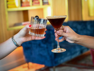 Two hands clinking cocktails—one with an Old Fashioned, the other with an espresso martini—capturing celebratory energy and guest experience in NYC hospitality marketing.
