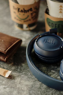 Blaue JBL-Kopfhörer liegen neben zwei Kaffees zum Mitnehmen auf einem Marmortisch