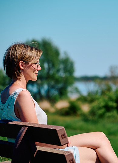 Katharina Günter sitzt nachdenklich auf einer Bank und blickt auf einen See, sonniger Sommertag