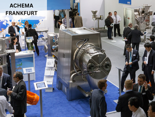 People in suits at a busy industrial expo in Frankfurt. Machinery displayed on blue carpet. Sign reads ACHEMA FRANKFURT.