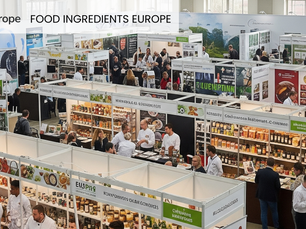Busy trade show with people interacting at food booths. Displays of packaged goods. "FOOD INGREDIENTS EUROPE" text at top. Bustling mood.