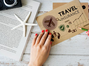 Hands with red nails examine a travel insurance brochure on a rustic table, alongside a book, starfish, and camera.