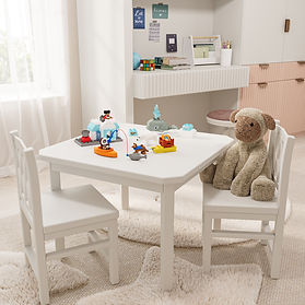 Tavolino bianco per bambini con sedie abbinate, decorato con giocattoli e un peluche. Scrivania e scaffali sullo sfondo con l