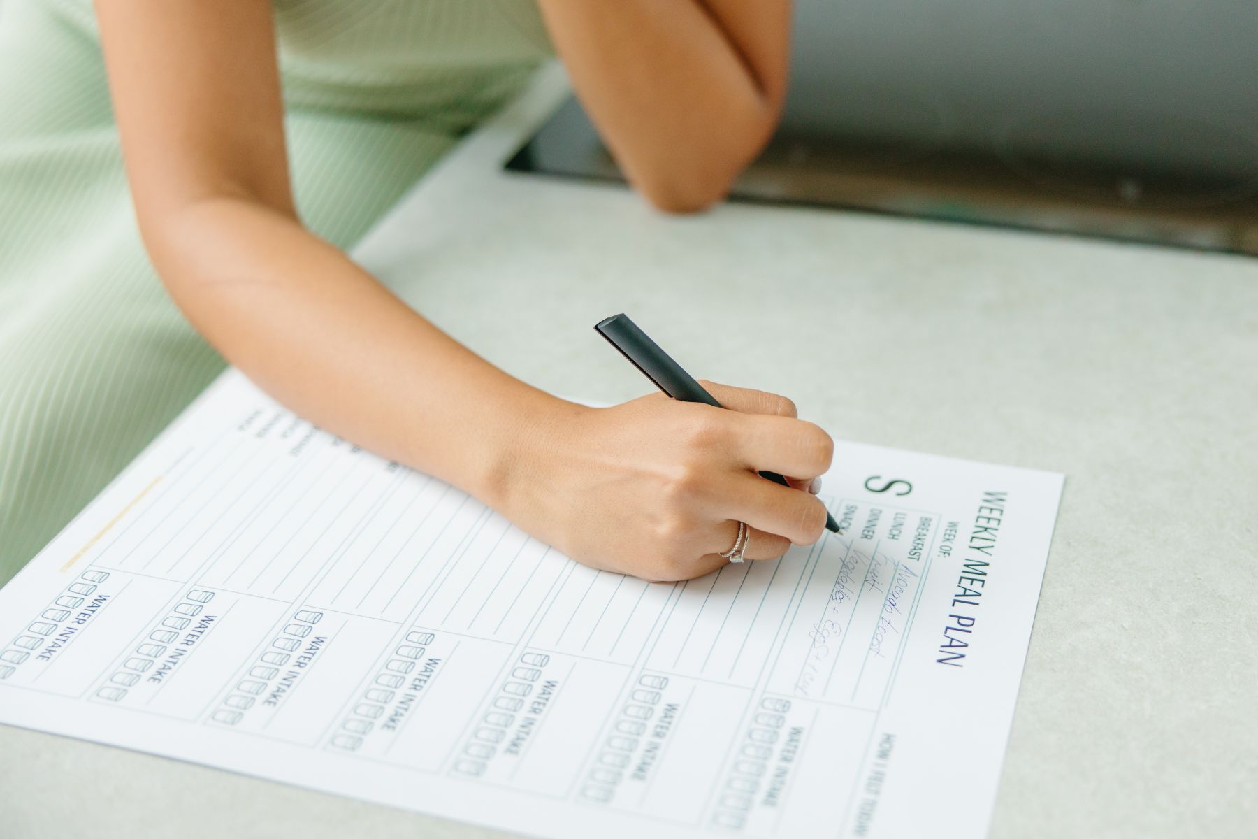 Women in green dress sitting at the kitchen table planning her intuitive eating meal plan on paper