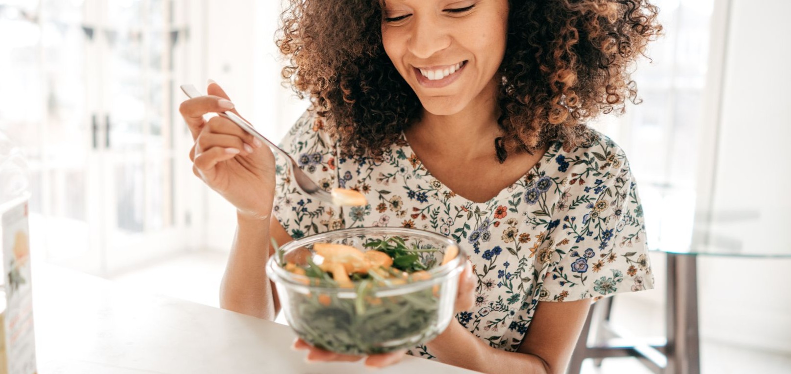 Women  smiling sitting a kitchen table intutitive eating and enjoying a healthy salad with a glass of water