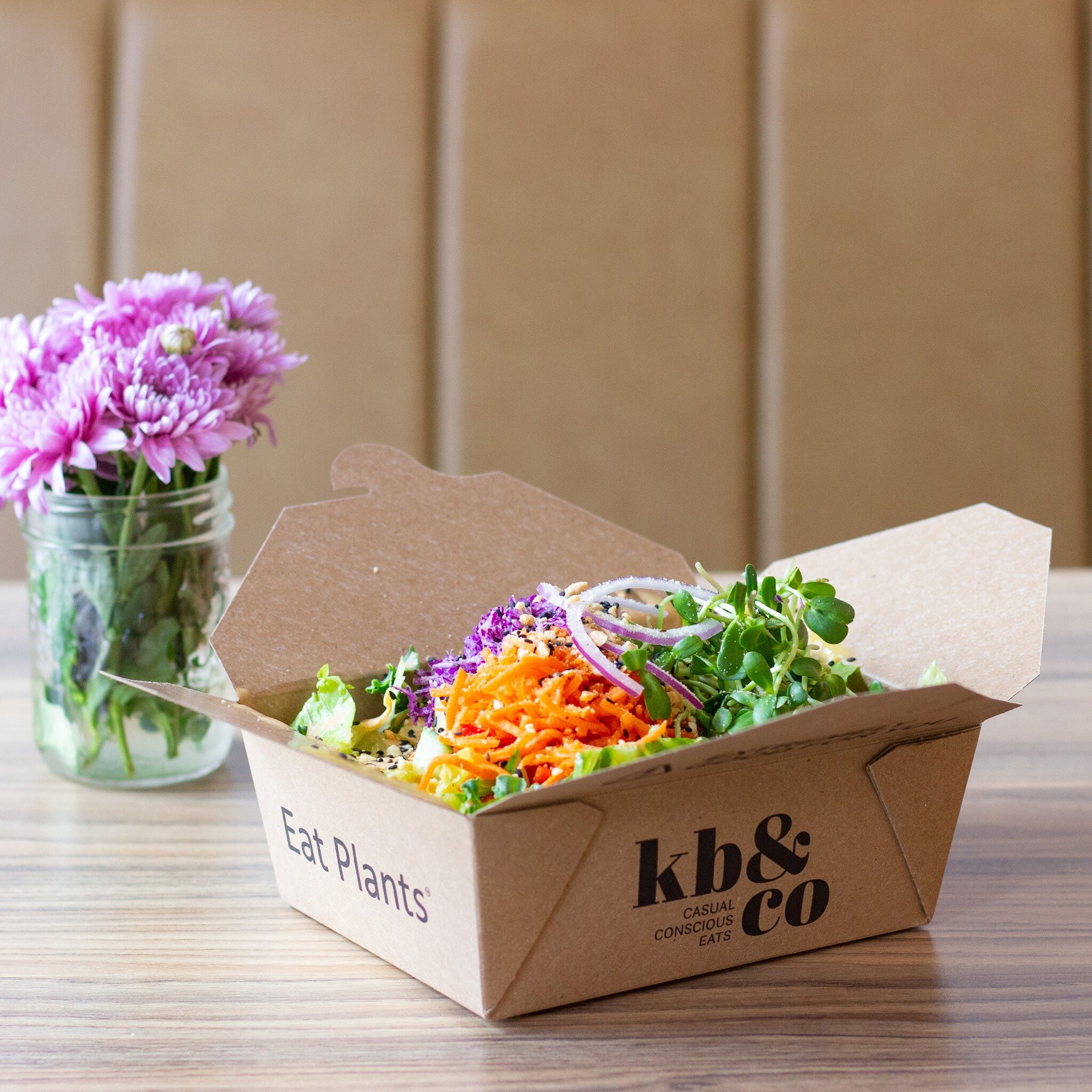 Kb & Co. takeout container filled with a grain bowl and loaded with colourful vegetables including purple cabbage, red pepper, cucumber, carrots and micro-greens