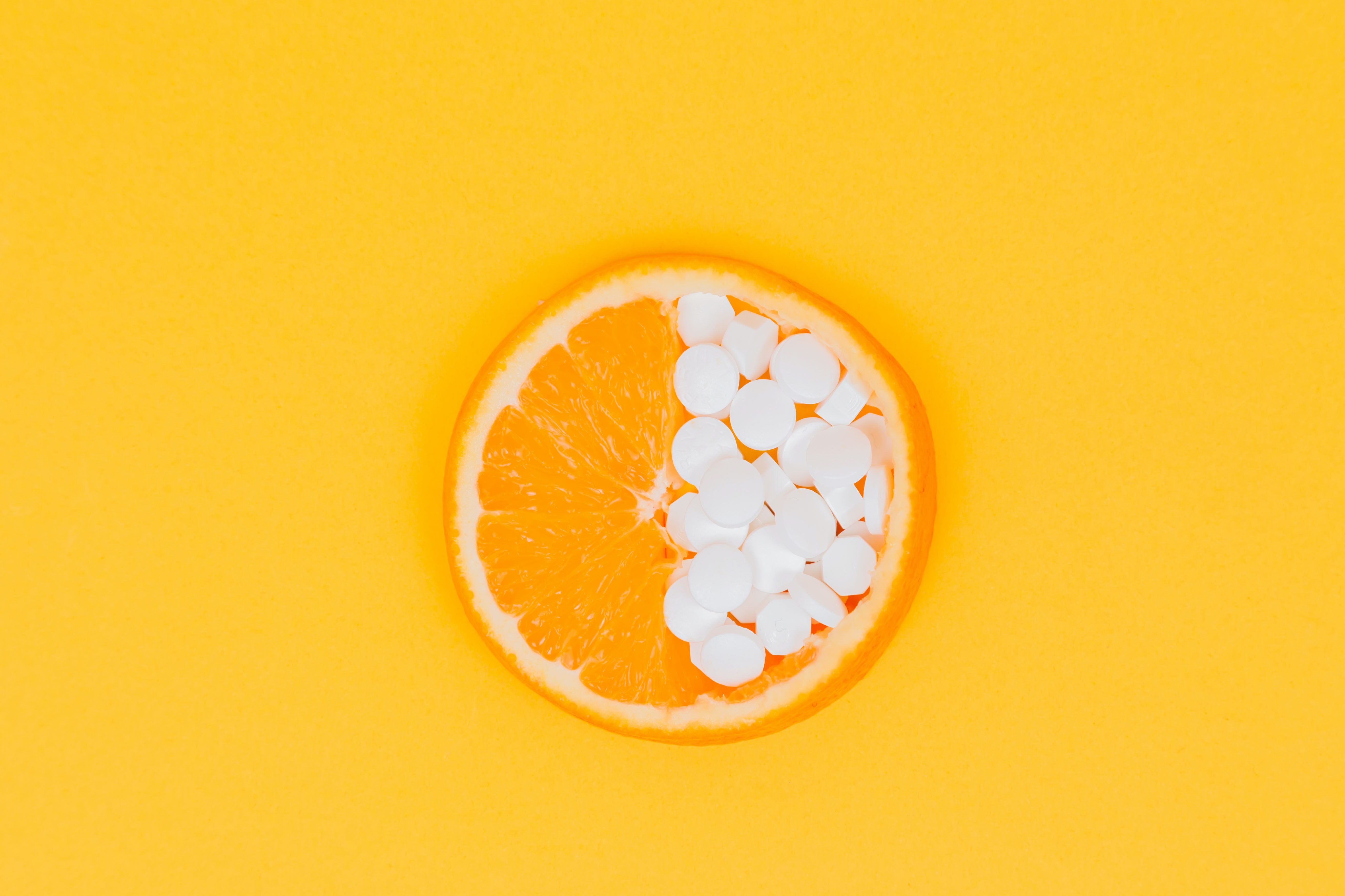 yellow background with a orange sliced in half with flesh facing up - half is the citrus fruit and other half is filled with vitamin C supplement