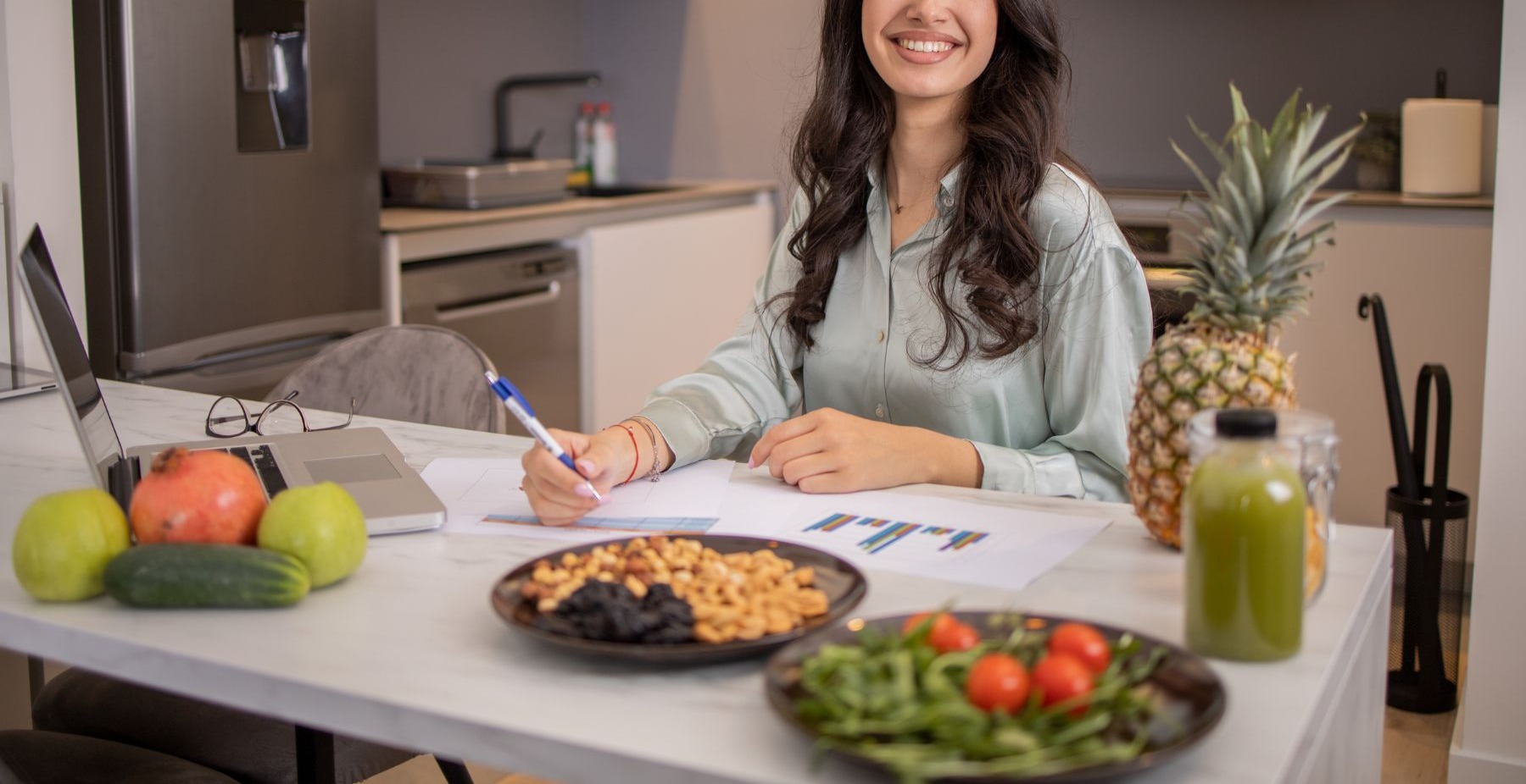 Dietitian smiling at kitchen counter with laptop, healthy food providing virtual nutrition care