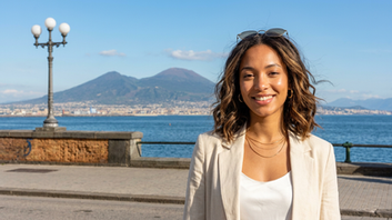 Donna italo‑afrodiscendente con lob mosso castano espresso sul lungomare di Napoli, mare e Vesuvio sullo sfondo.